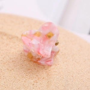 Macro shot of a pink marble acetate heart hair claw clip with golden metal spring