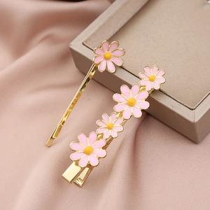 Détail de barrettes marguerites roses sur satin avec finition dorée et pétales émaillés