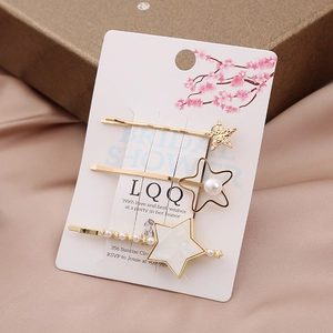 Elegant gold star hair clip set with white pearls and rhinestones on a card display