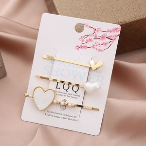 Three-piece golden heart hair clip set with pearls and rhinestones on card display