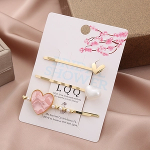 Three-piece heart hair clip set with pink marble and pearl accents on elegant card