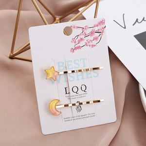 Detail of star and moon enamel hair clips set in gold finish on floral card