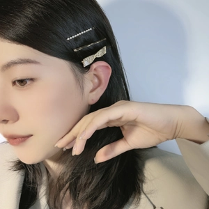 Detailed view of hair clip set featuring pearls, gold pin, and rhinestone bow on model