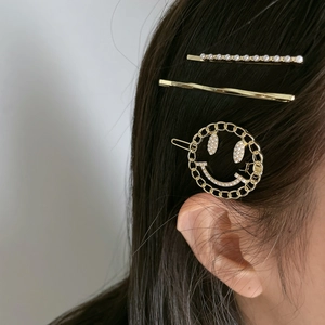 Close-up of golden hair clip set featuring pearl smiley face and minimalist metal designs