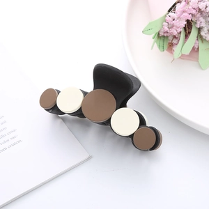 Close-up of a matte black hair claw clip with brown and cream circular accents