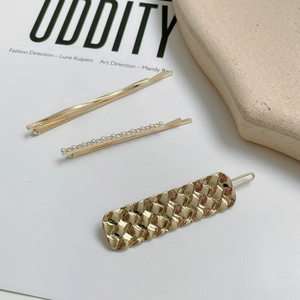 Close-up of three gold hair clips featuring a wavy bar, pearls, and a woven metal texture