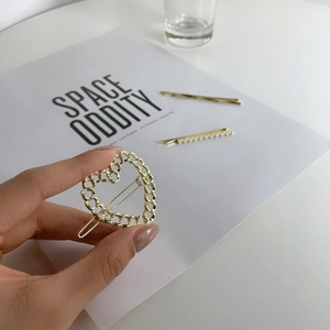 Detail of gold heart chain hair clip with pearl bobby pins held by hand