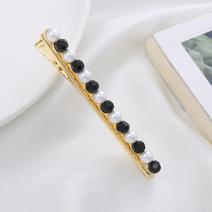 Elegant gold hair clip with pearls and black crystals on white fabric background