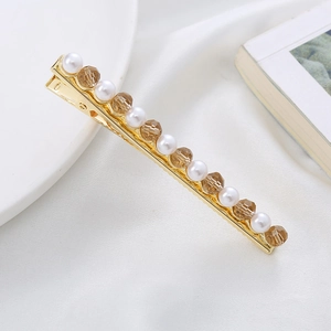 Detail view of a gold hair clip with pearls and amber crystals on white fabric