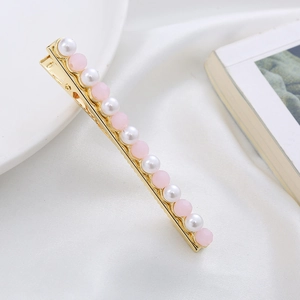 Elegant gold metal hair clip with pink and white pearl beads on white ceramic tray