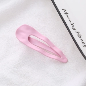 Macro view of a matte pink teardrop hair clip with wavy texture on white linen
