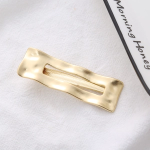 Detail of matte gold rectangular hair clip with wavy texture on white fabric
