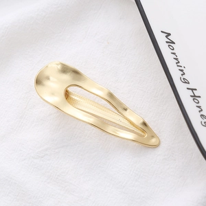 Minimalist irregular wave hollow gold hair clip for women on a white textured fabric