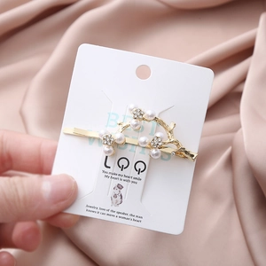 Elegant gold twig hair clip with pearls and rhinestones on a decorative display card