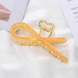 Detail of gold metal shark hair claw clip with orange marble pattern on silk background