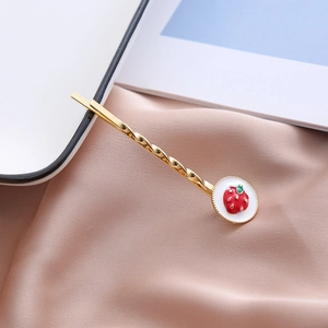 Détail d'une pince à cheveux fraise dorée sur tissu en soie rose avec émail rouge