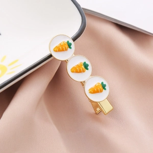 Gros plan détaillé d'une barrette dorée avec breloques carottes en émail blanc et feuilles vertes