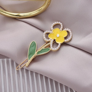 Eleganter gelber Blumen-Haarclip mit Perlen und grünen Blättern auf Seidenhintergrund