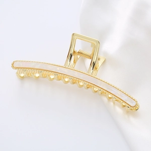Large gold metal hair claw clip with white pearlescent inlay on elegant white silk background