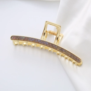 Close-up of a large gold metal hair claw with dark tortoiseshell acetate wavy patterns