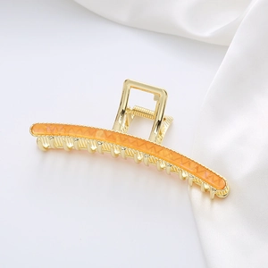Close-up of golden alloy shark hair claw clip with orange translucent patterned inlay