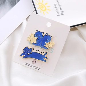 Detail view of two blue enamel cat pins with gold stars on white satin background
