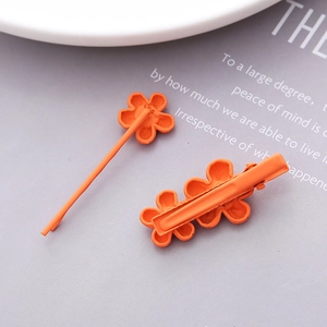 Detail view of orange floral hair clips with matte finish on purple aesthetic background