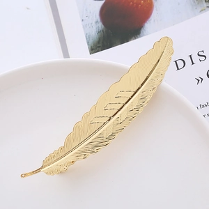 Elegant gold metal feather hair clip with detailed leaf texture on white ceramic tray