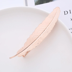 Rose gold feather hair clip with metallic texture on white plate for elegant hair styling