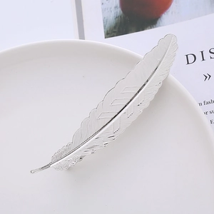 Detailed close-up of a silver metal feather hair clip with fine texture on white porcelain