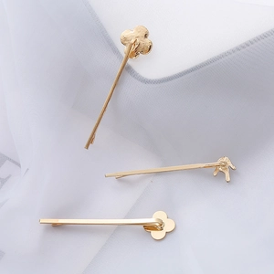 Detail von drei goldenen Haarspangen mit Kleeblatt- und Handgesten-Design auf weißem Tüll