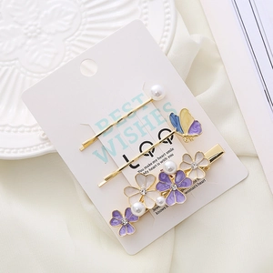 Detail of floral hair clip set with purple enamel flowers, pearls, and butterfly decor