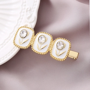 Elegant gold tulip hair clip with white enamel and sparkling crystals on purple fabric