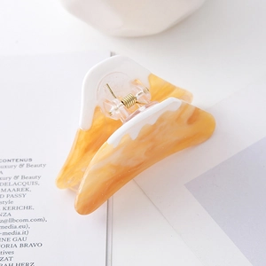 Macro detail of amber acetate hair claw with white wavy gradient and gold spring