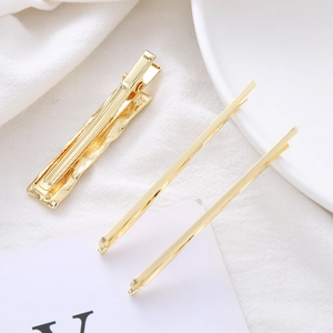 Detail of three gold geometric hair clips with wave texture on a clean white fabric