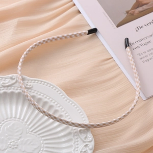 Detail of thin beige gingham fabric headband with protective black ear tips on smooth pink fabric