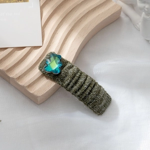 Dettaglio di un fermaglio per capelli in maglia verde scuro con orsetto di strass blu