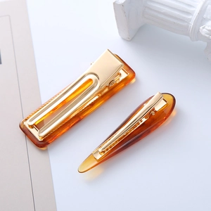 Detail of amber tortoiseshell acetate hair clips with gold metal base on stone pedestal