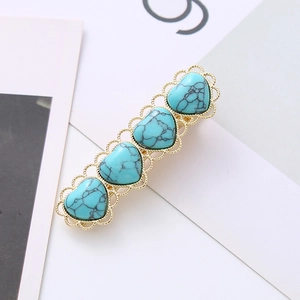 Detail of four turquoise heart stones in golden lace settings on a metal hair clip