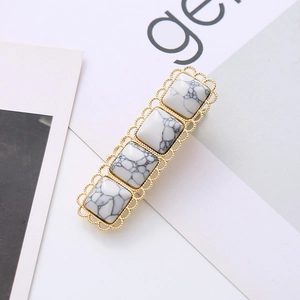 Detailed close-up of a golden lace metal hair clip inlaid with white marble textured stones