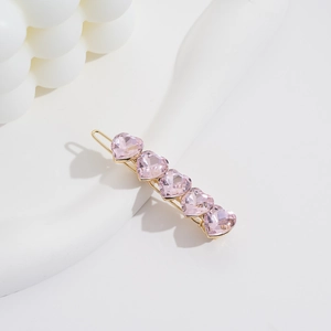 Minimalist gold hair clip with five pink heart-shaped crystals on white aesthetic props