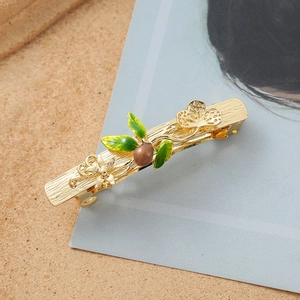 Close-up of golden butterfly hair clip with green enamel leaves and floral details