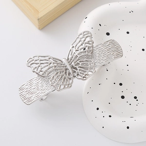 Silver hollow butterfly bow hair clip with rhinestones on a white ceramic display plate