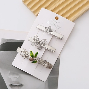 Detailed view of silver butterfly and floral hair clip set with green enamel leaf accent