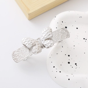 Close-up of a silver hollow butterfly hair clip with textured metal on a ceramic tray