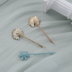 Dettaglio di tre forcine per capelli a margherita con finitura dorata e trama blu chiaro