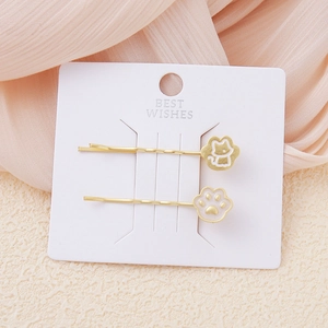 Detalle de las pinzas para el cabello con diseño de gato dorado y huella en tarjeta