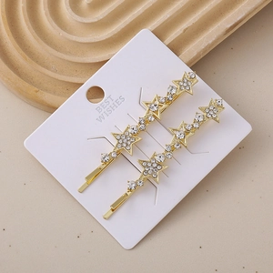 Detailed macro view of two gold star hair clips with sparkling rhinestones on a card