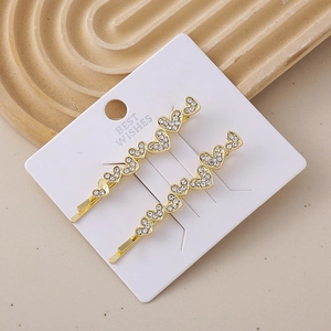 Detail of two gold-toned heart-shaped hair clips with sparkling rhinestones on display card