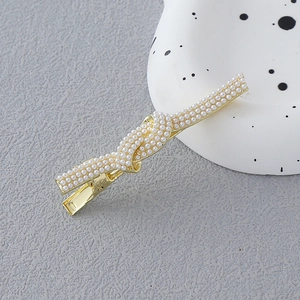Détail d'une pince à cheveux dorée avec perles blanches et design de nœud torsadé